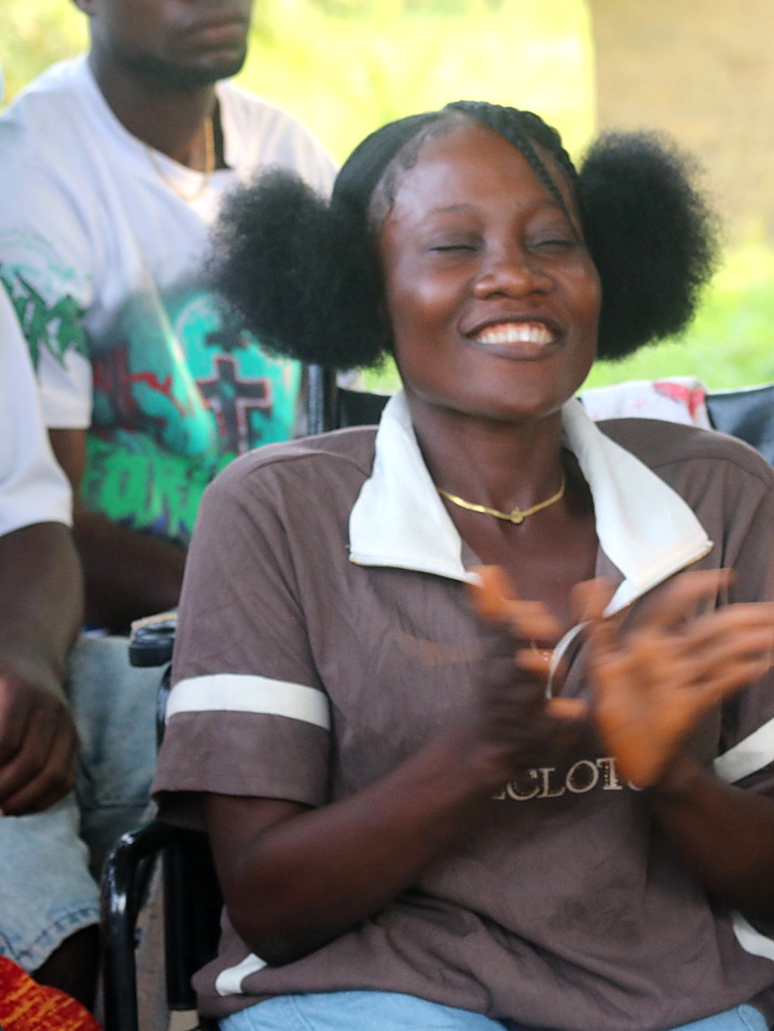 A young woman using a wheelchair applauds during a community meeting on disability inclusion.