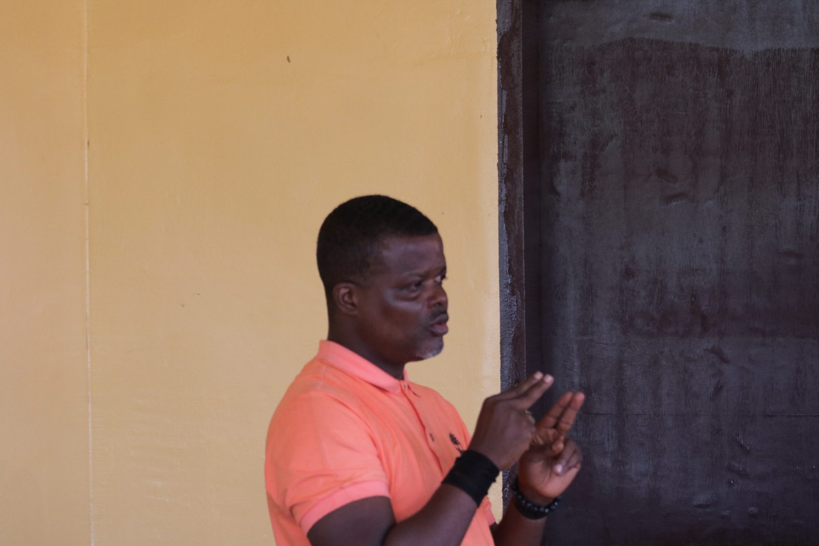 A man signing in Liberian sign language while addressing a room of community members.