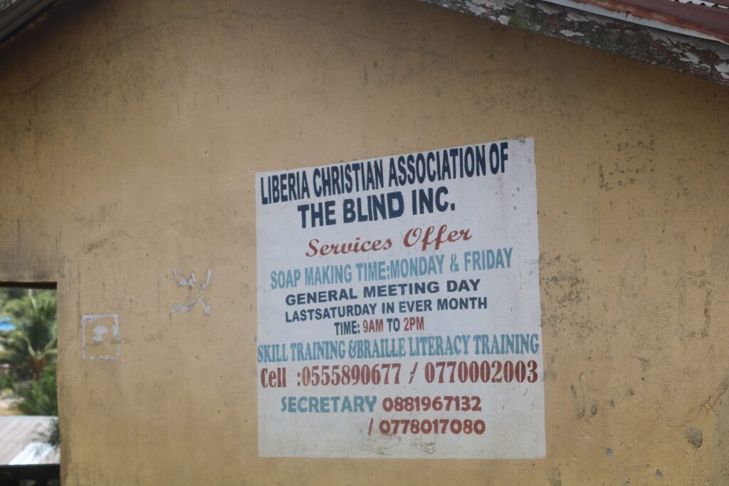 A painted signboard for the Liberia Christian Association of the Blind, listing skills training and Braille literacy training.