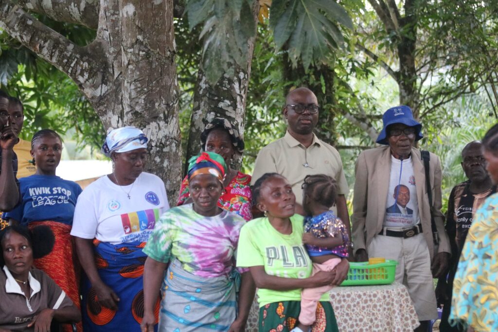 Community members and Commission staff standing together under trees during a county visit.