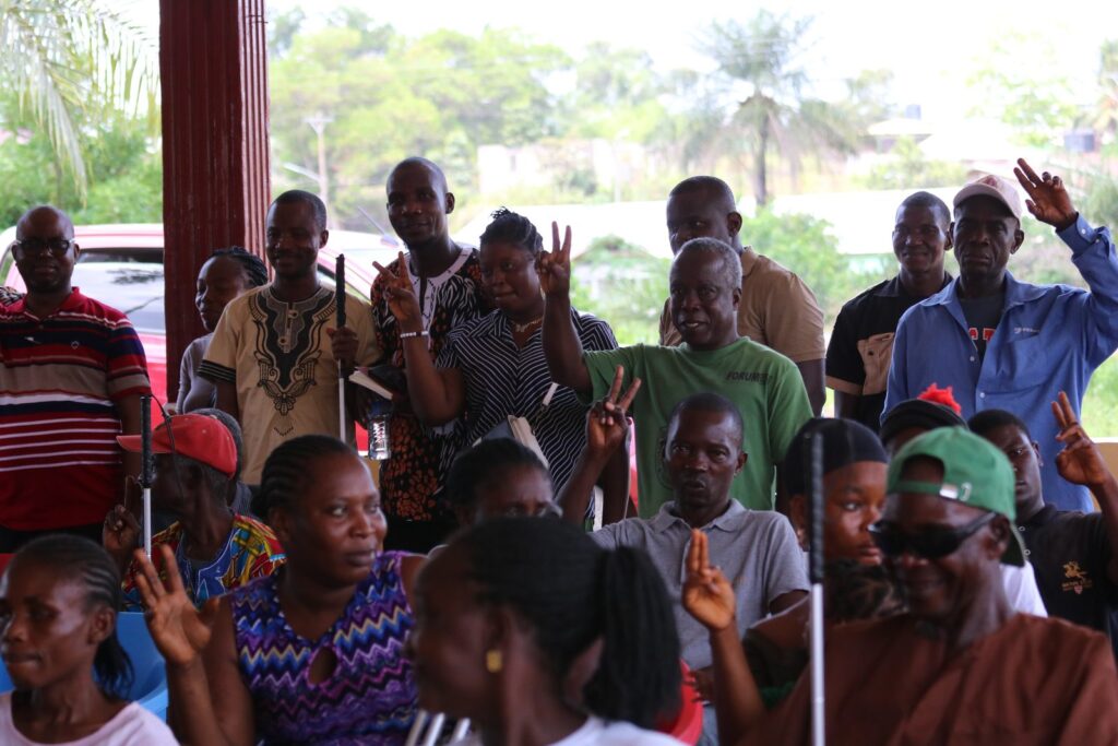 Community members raising their hands during an outreach session held under an open shelter.
