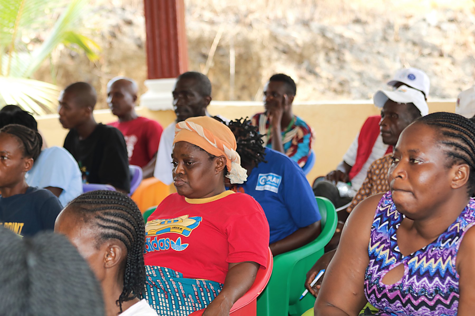 Community members seated on green chairs listening during an outdoor session.