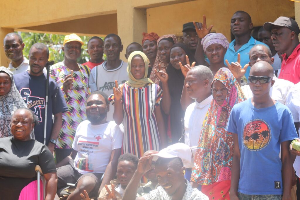 A large group of persons with disabilities and Commission staff gathered outside a community building.