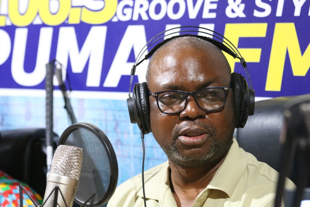 A man wearing headphones speaks into a studio microphone at a community radio station.
