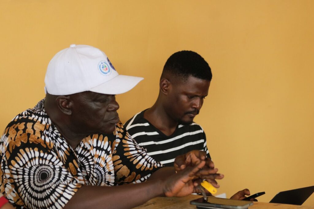 Two men seated at a table, one writing down details from the other.
